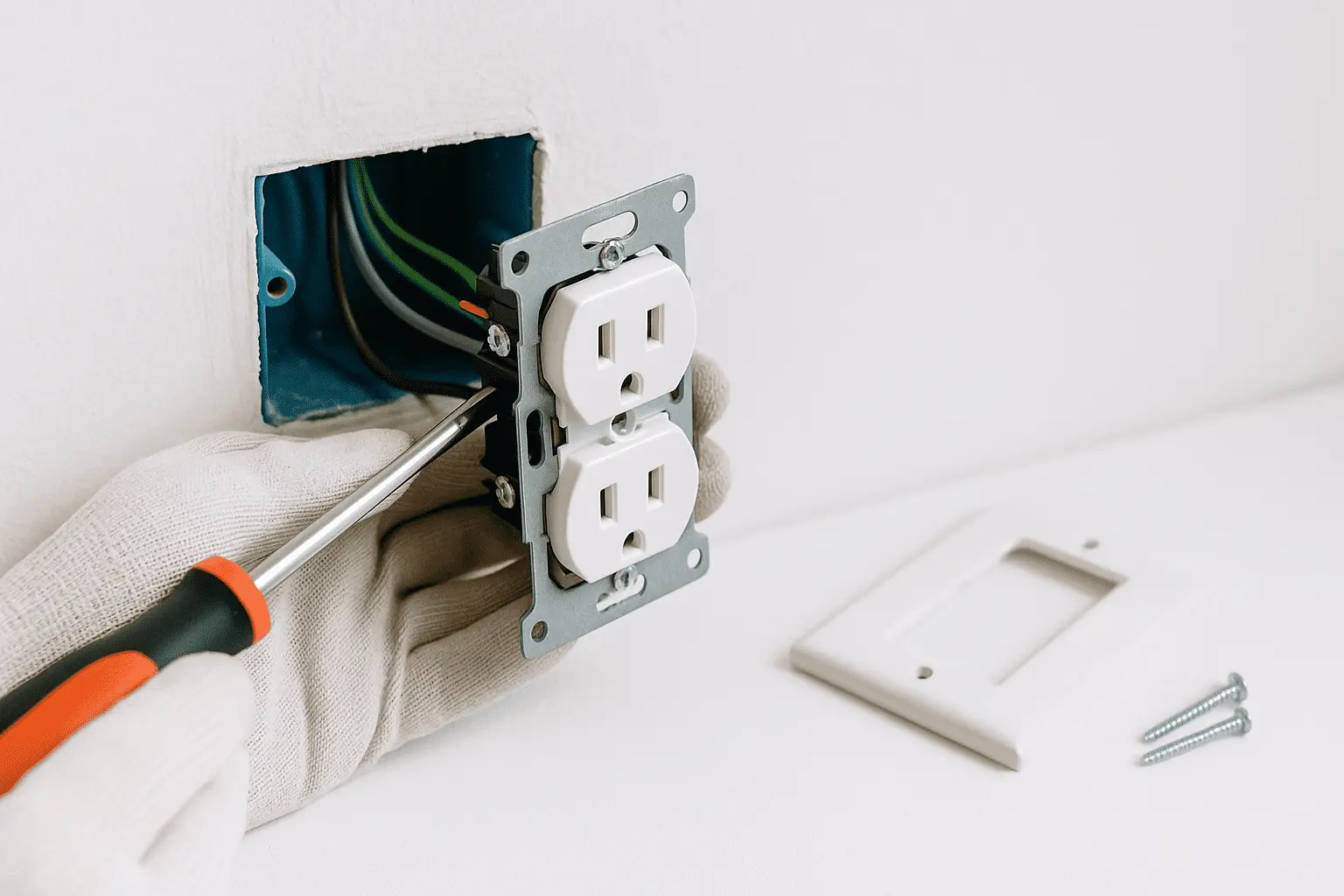Instalación real de enchufe doble empotrado en caja 2×4, técnico ajustando bastidor con destornillador; cables 2,5 mm² ordenados y placa lista.