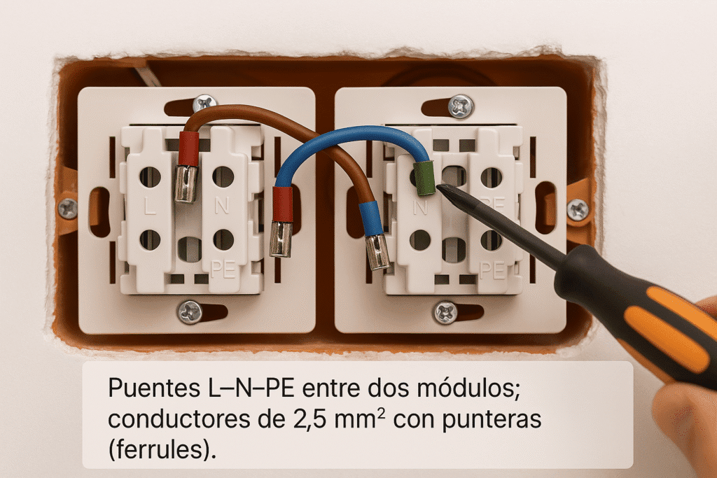Primer plano real del interior de una caja 2×4: dos tomas modulares lado a lado con bornes marcados L, N y tierra; puentes cortos de 2,5 mm² (marrón, azul y verde‑amarillo) unen ambas tomas, y un destornillador dinamométrico ajusta los tornillos.