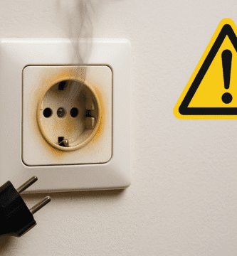 Enchufe de pared con marcas de quemado y humo, clavija desenchufada y símbolo de advertencia.