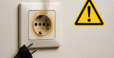 Enchufe de pared con marcas de quemado y humo, clavija desenchufada y símbolo de advertencia.