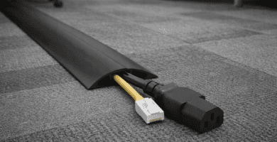 Pasacables de piso de perfil bajo protegiendo cable de alimentación y Ethernet sobre alfombra de oficina.