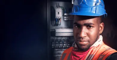 Electricista con casco y lentes de seguridad frente a un tablero eléctrico