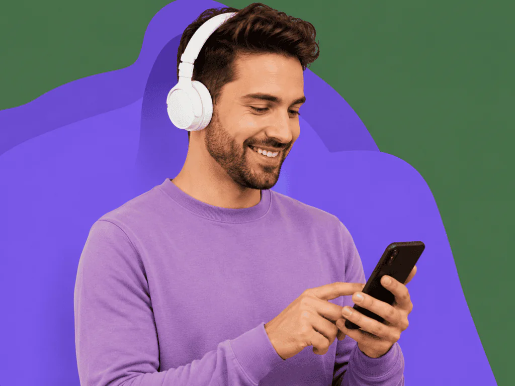 Hombre sonriendo con auriculares mientras usa su celular sobre fondo morado moderno